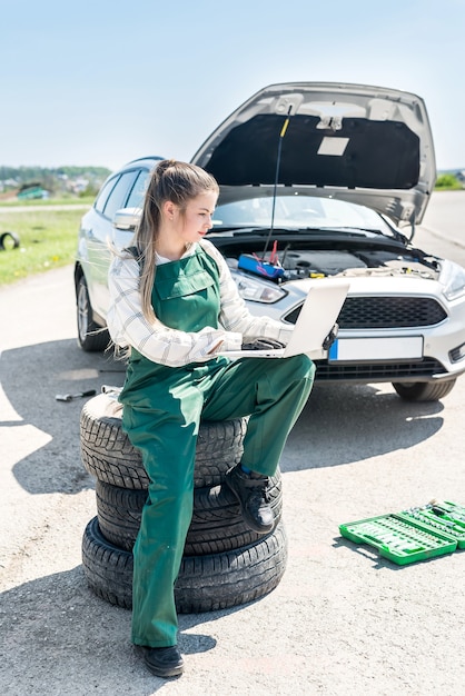 Woman mechanic with broken car and laptop