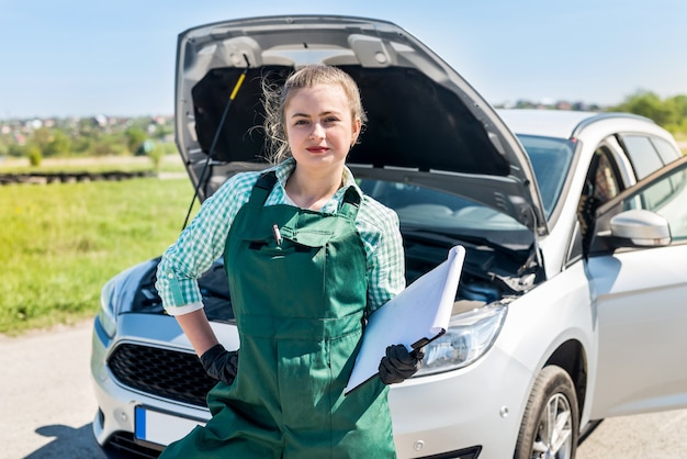 Woman mechanic with clipboard and broken car