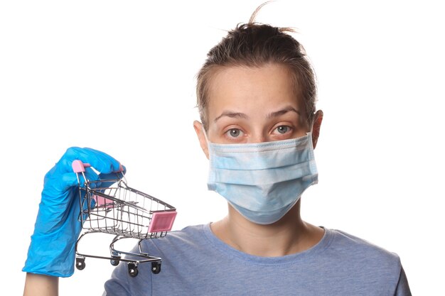 Woman in media mask and gloves holds shopping trolley isolated on white