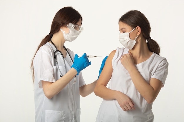 woman in medical clothes on a white background with a vaccine and a syringe makes a vaccination