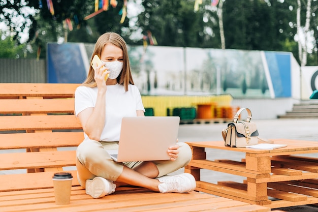 woman in medical face mask talking over the phone outdoors