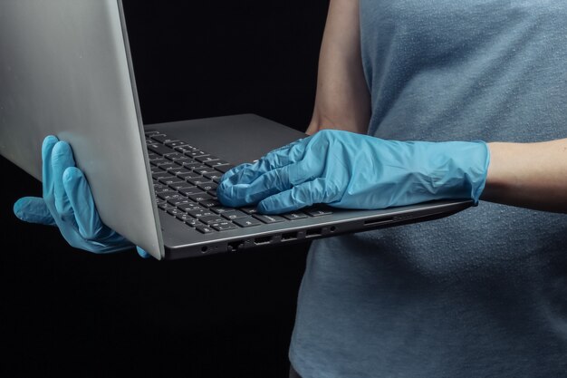 Woman in medical gloves holds a laptop on a black wall.