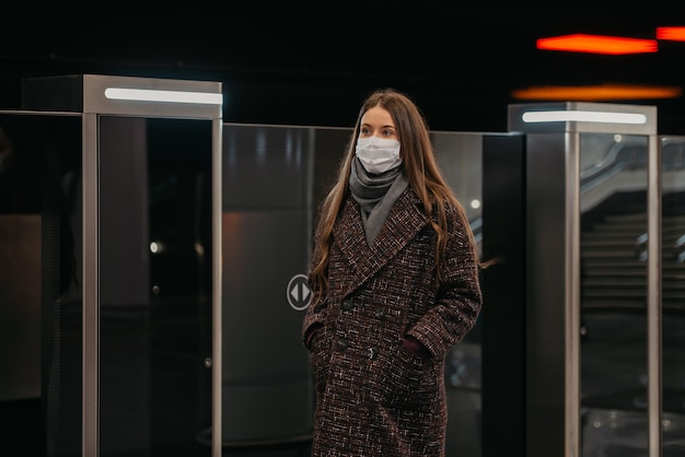 Una donna con una maschera medica per evitare la diffusione del coronavirus è in piedi vicino al treno in partenza sulla piattaforma della metropolitana. una ragazza con una mascherina chirurgica sta mantenendo le distanze sociali in una stazione della metropolitana.