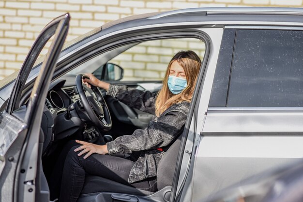 woman in medical mask driving a car, looking at the camera because air pollution