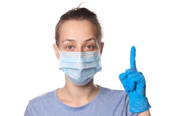 Woman in medical mask and gloves raises index finger up. Isolated on white.