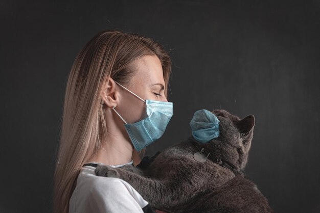 의료용 마스크를 쓴 여성이 영국 고양이를 팔에 안고 고양이도 의료용 마스크를 쓰고 있습니다