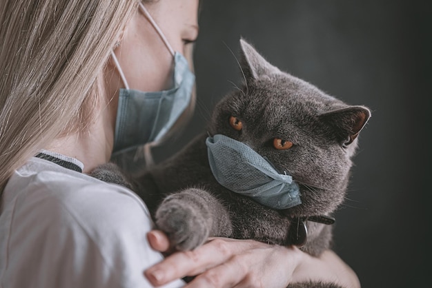 A woman in a medical mask holds a British cat in her arms the cat is also in a medical mask