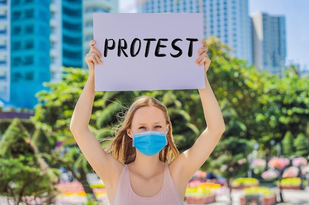 의료용 마스크를 쓴 여성이 코로나바이러스 질병을 예방하고 손으로 쓴 텍스트에 항의하는 포스터를 들고 있다