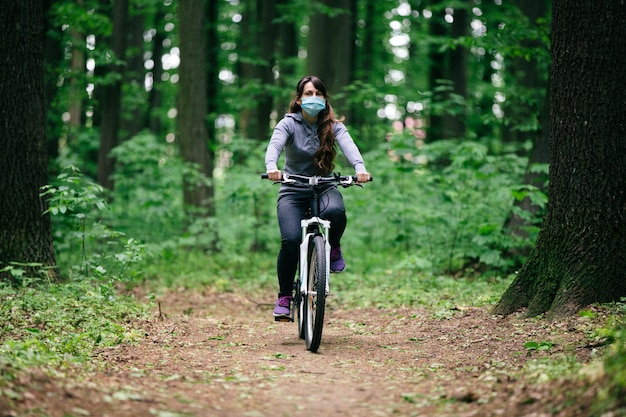 Woman in medical mask rides a bicycle in the park