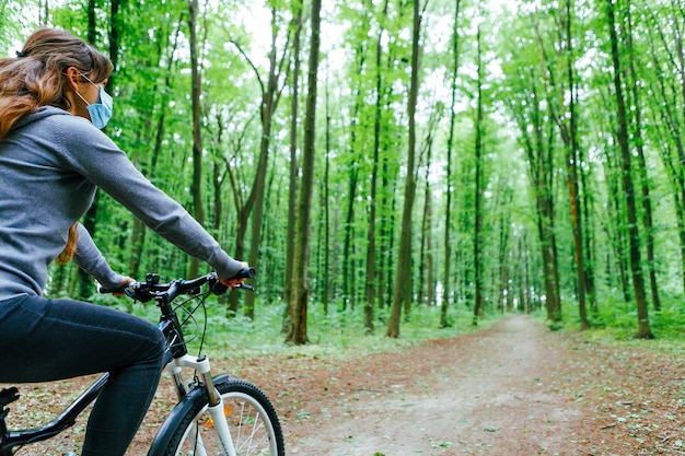 Woman in medical mask rides a bicycle in the park