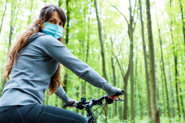 Woman in medical mask rides a bicycle in the park