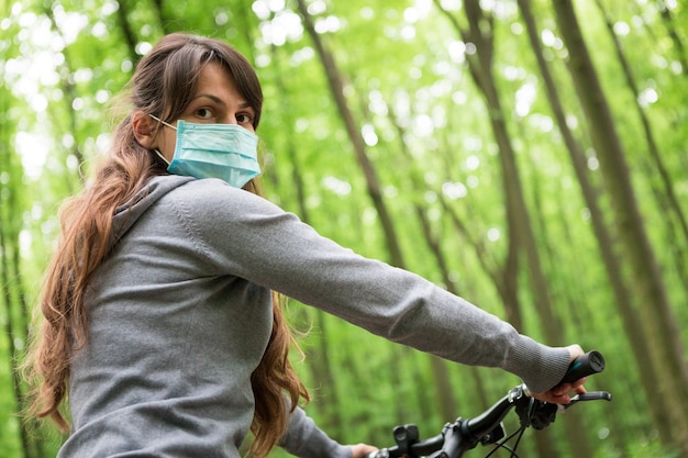 Woman in medical mask rides a bicycle in the park