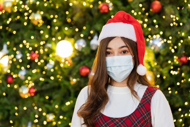 Woman in medical mask and santa cap with Christmas tree, coronavirus(covid-19) and x-mas celebrating concept