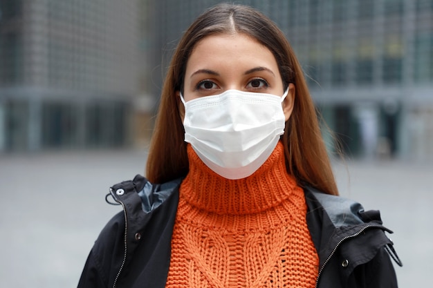 Woman in medical mask standing in empty modern city street looking at camera