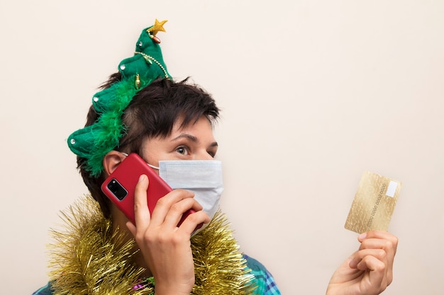 Woman in medical mask wearing a Christmas tinsel with smartphone and credit card