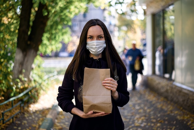 Woman in medical mask with paper bag in hands on street, safe shopping concept, donate