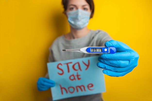 Woman in a medical mask with a temperature. holding a thermometer in his hands. mild condition of a coronavirus patient. stay home