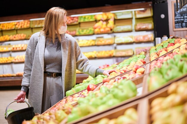 医療マスクの女性は、ウイルスのパンデミック中に食料品店で買い物をしています