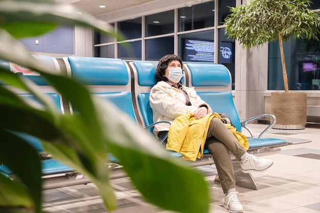 Woman in a medical protective mask sits in the departure area of the airport and waits for the start of boarding