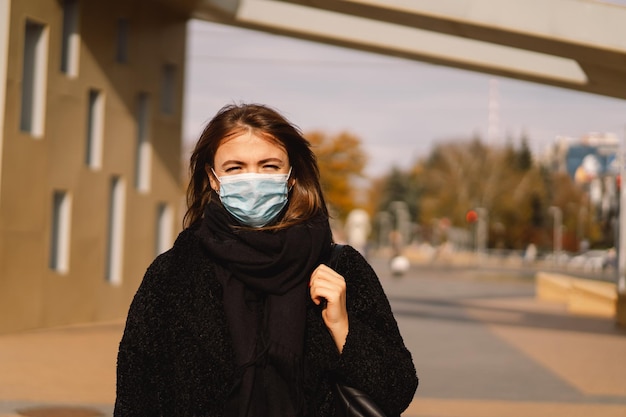 A woman in a medical protective mask walks down the street in the city. Covid pandemic time in Europe and in the world. Safety for people.