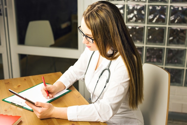 Woman medicine doctor hold jar of pills and write prescription to patient at worktable