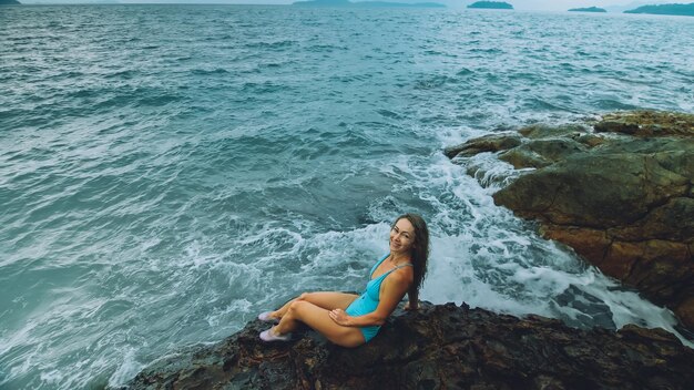 Photo woman meditates relaxes on a rock reef hill in stormy morning rain cloudy sea