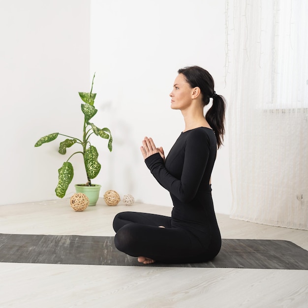 A woman meditates sitting in a lotus position with namaste trains in black sportswear