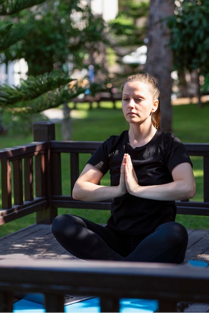 A woman meditates in a yoga lotus position on her porch at home\
black porch and clothes against the...