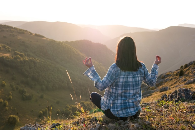 山と夕日に対して瞑想する女性