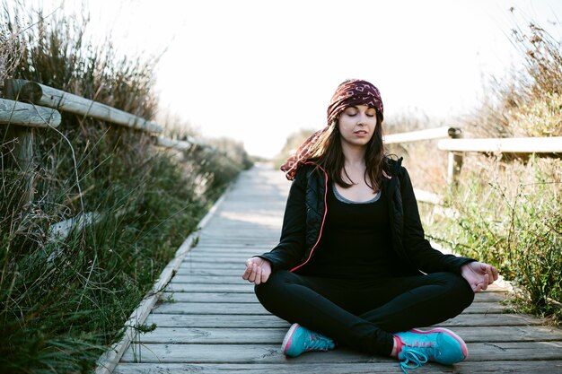 Photo woman meditating on boardwalk amidst grass