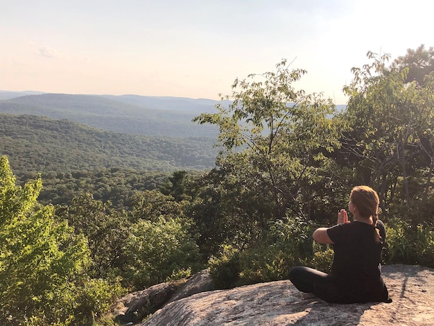 Foto donna che medita su una scogliera contro le montagne durante il tramonto