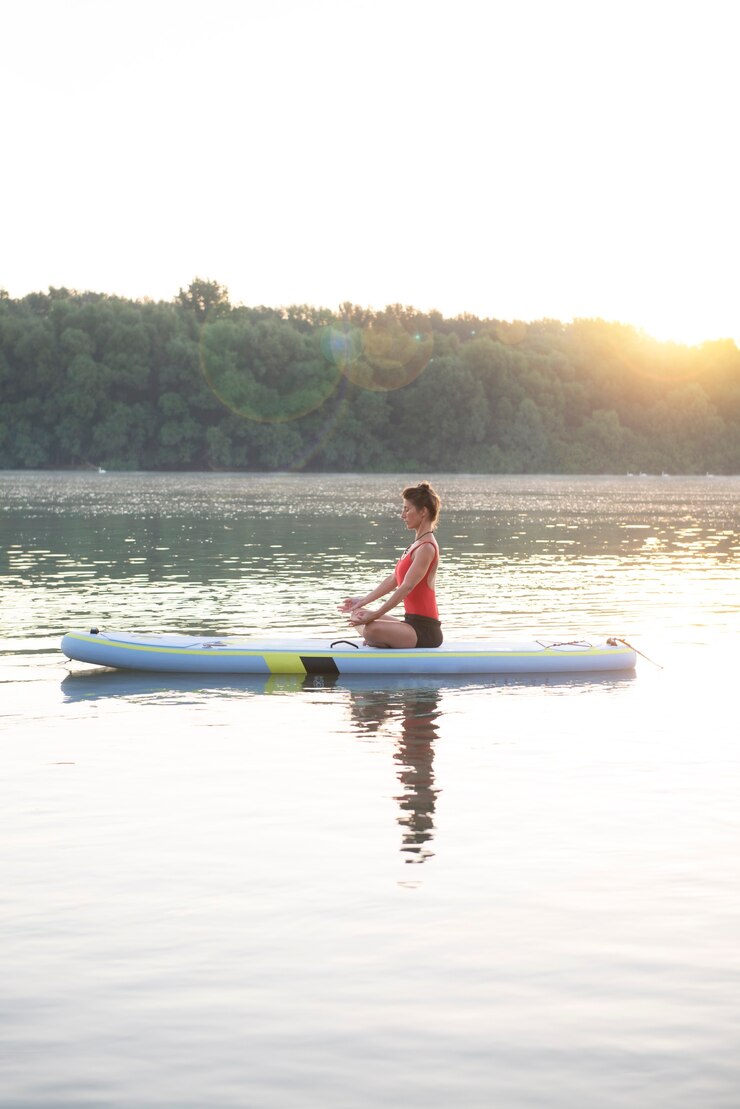 Woman meditating and practising yoga during sunrise in paddle board