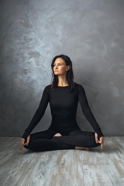 Woman meditating while sitting in a lotus position near a wall with an abstract pattern