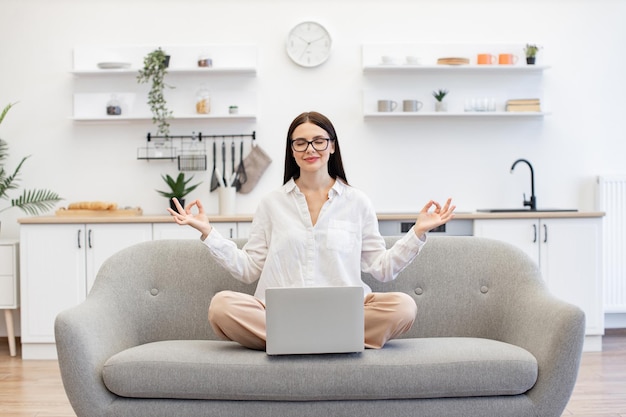 Woman meditating while working on portable laptop at living room