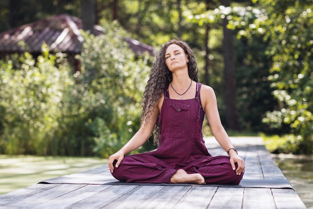 A woman meditating with her eyes closed sitting in a lotus position on a wooden bridge