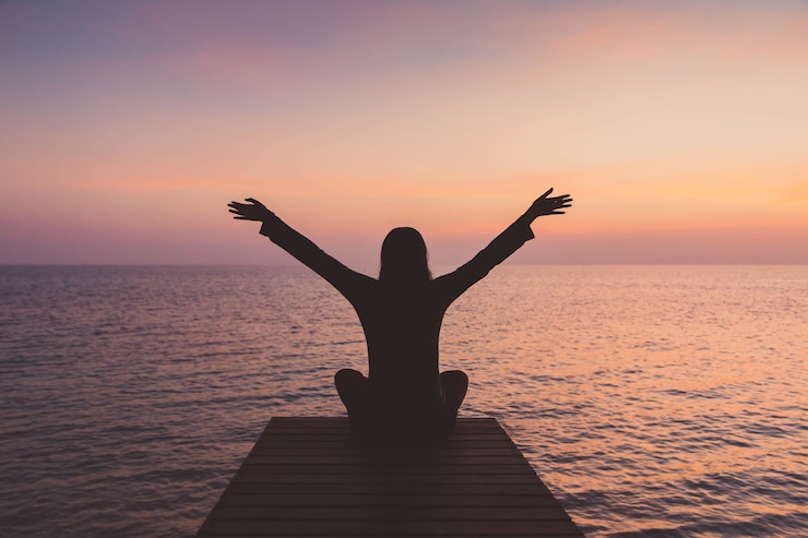 Photo woman meditating on a wooden bridge and rising hand by the sea 