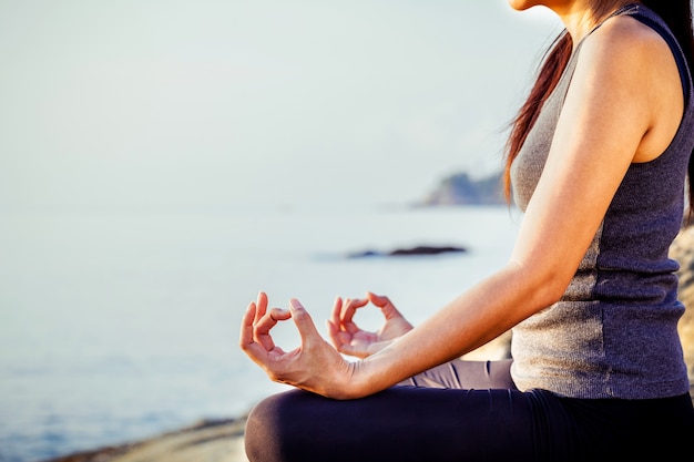 The woman meditating in a yoga pose on the tropical beach. 