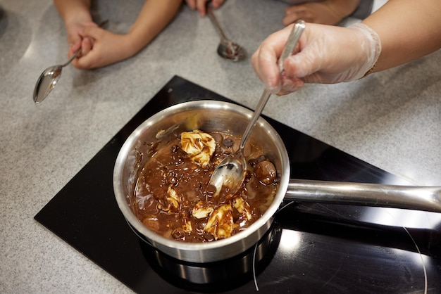 鍋にチョコレートを溶かし、バターと混ぜる女性、クローズアップ。家庭料理、自家製の甘い食べ物。