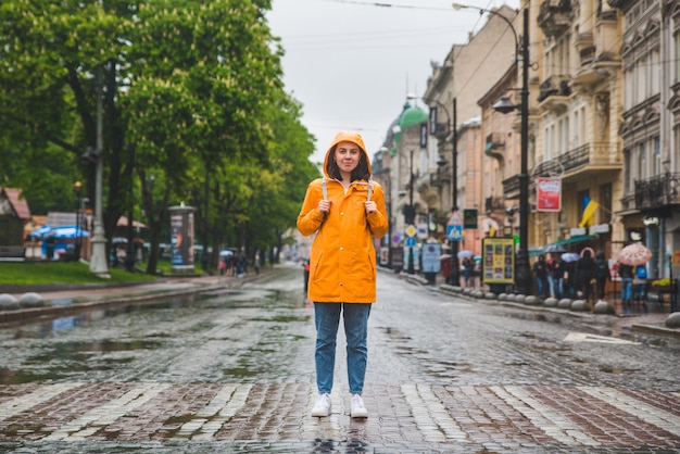 Женщина посреди улицы переходит дорогу в желтом плаще