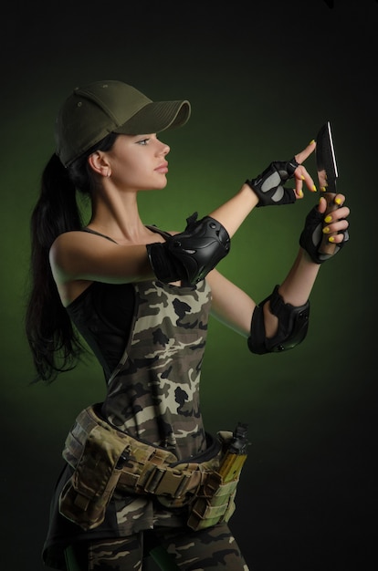 Woman in military special clothes posing with a gun in his hands on a dark wall in the haze