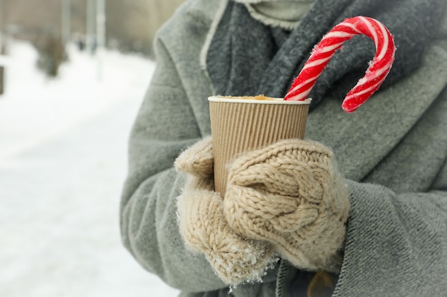 Woman in mittens hold cup of hot drink outdoor in winter