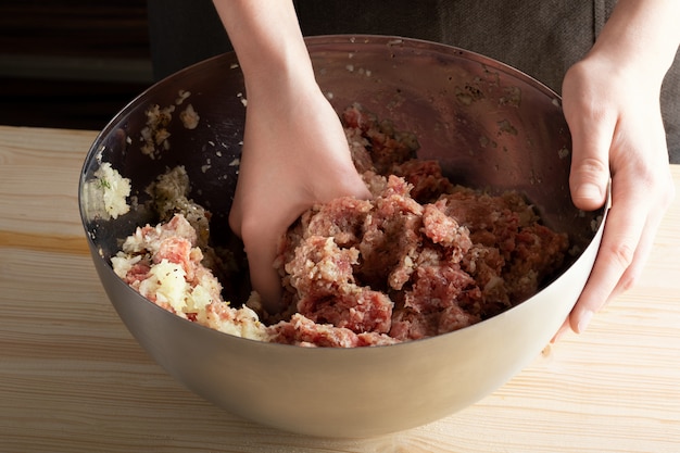 写真 女性は、金属製のボウルにミンチ肉を混ぜます。ミンチ肉を調理するプロセス。餃子またはラビオリのステップバイステップのレシピ、ステップ1。クローズアップ。