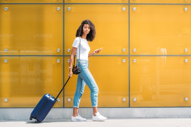 Woman on the mobile phone while walking with a suitcase