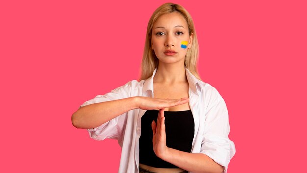 Woman of model appearance with the flag of Ukraine on her face holds posing on a pink background