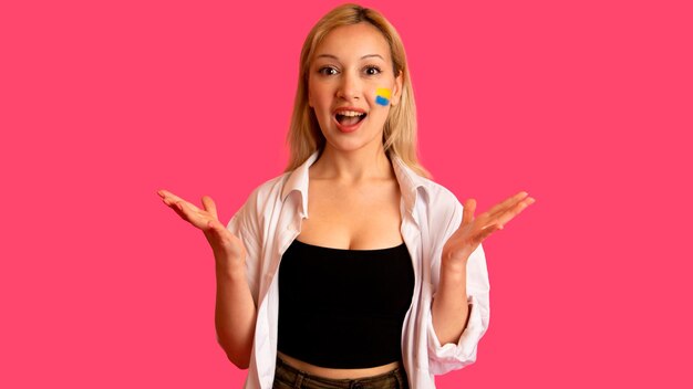 Woman of model appearance with the flag of Ukraine on her face holds posing on a pink background