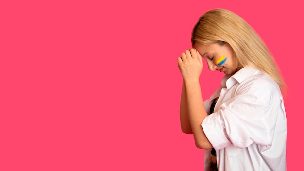 Woman of model appearance with the flag of Ukraine on her face holds posing on a pink background