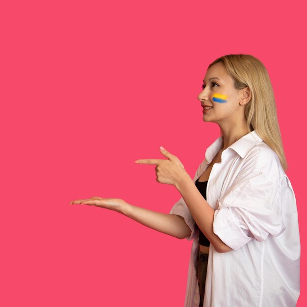 Woman of model appearance with the flag of Ukraine on her face holds posing on a pink background