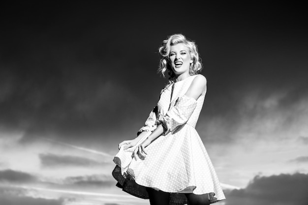 Woman in monroe dress on dramatic sky. Beautiful young woman in fashion dress outdoor. Sexy and sensual female model.