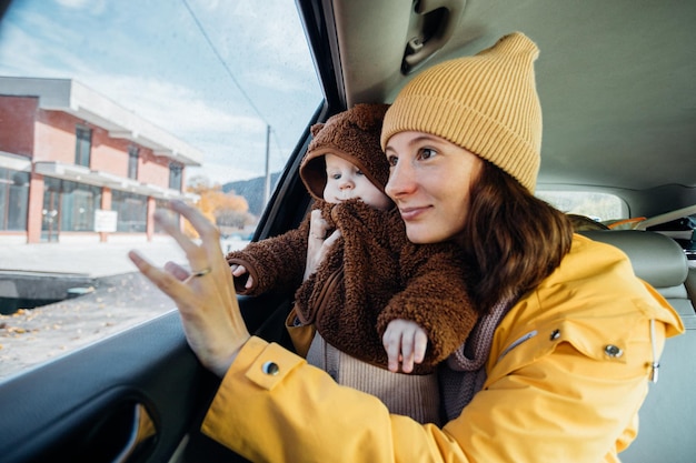 woman mother holds the baby in her arms and looks with him out the window from the car