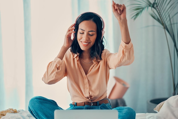 Photo woman music and bed with laptop dancing and headphones in bedroom relax and smile girl dance and room with streaming computer and listen on web internet and app for radio audio and technology